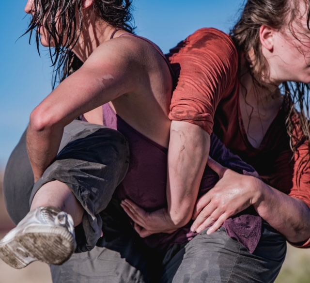 Two dancers intertwine their bodies into a tight not. Their faces are not visible, their sun soaked cheeks and windblown hair is.